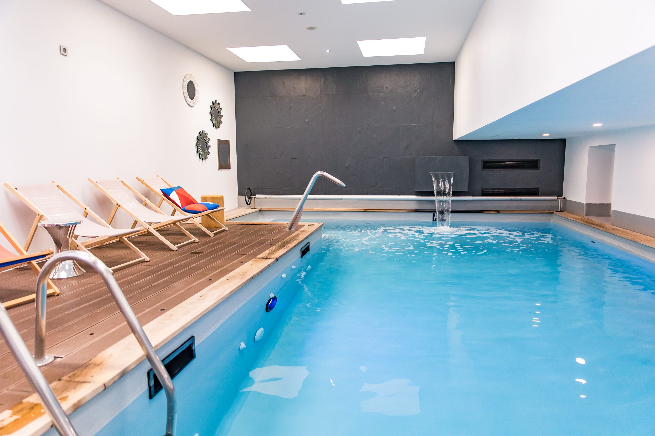 piscine intérieure éclairée avec chaises longues et mur décoratif - hotel spa finistere